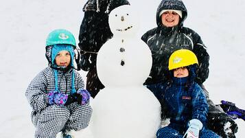 Tre barn sitter bredvid en snögubbe i en snötäckt utomhusmiljö.