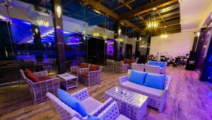 Ein geräumiger Lounge-Bereich mit Korbmöbeln, eine Bühne mit Musikinstrumenten und Blick auf die Stadt durch große Fenster.