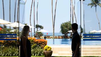 A man and a woman standing in a glass-walled area with a pool and palm trees in the background.
