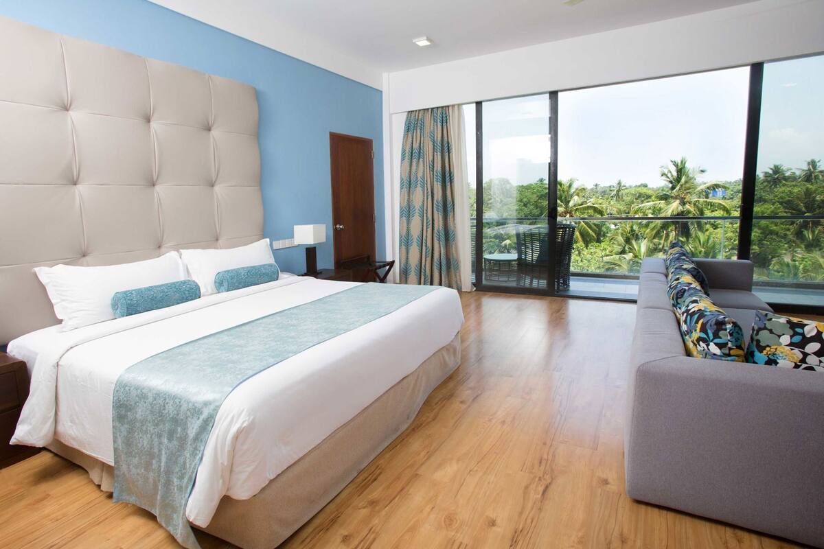 Une chambre d’hôtel moderne dotée d’un grand lit, d’un canapé, d’un balcon offrant une vue sur la verdure et d’un plancher en bois.