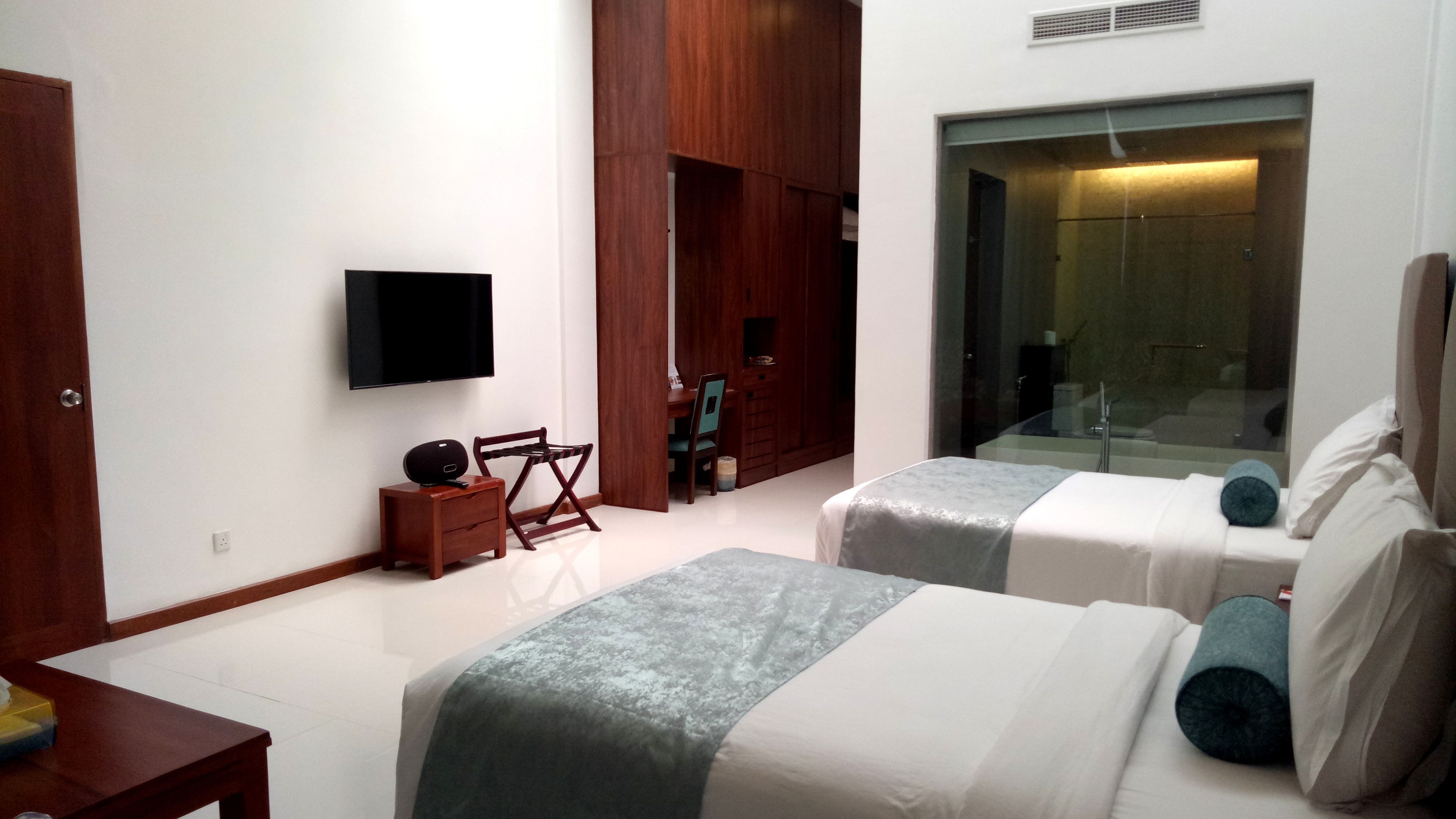 A modern hotel room with two beds, a TV, a small table, and a wooden wardrobe.