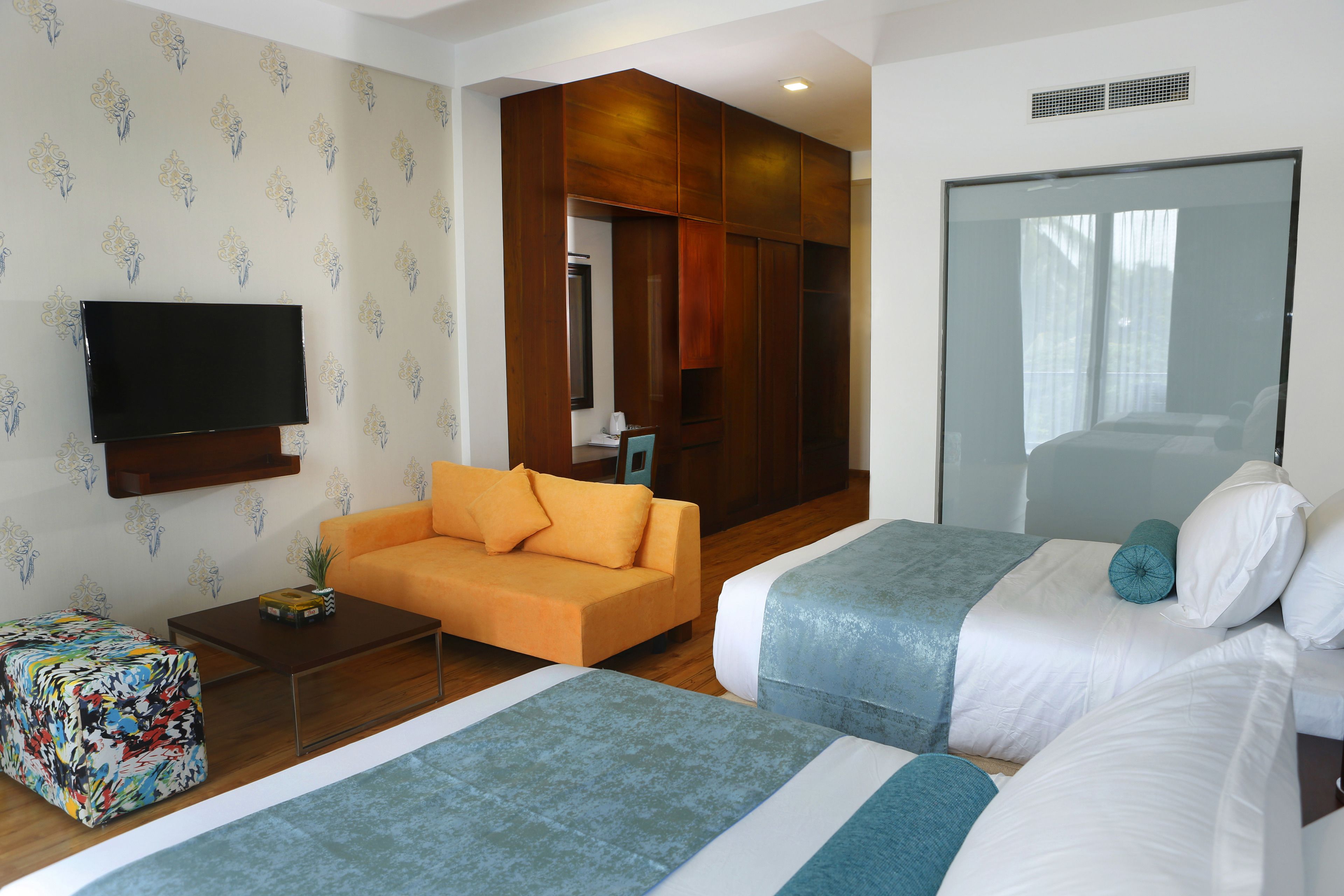 Quarto de hotel com duas camas, um sofá, uma televisão e um espelho.