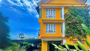 A two-story yellow building with a balcony, surrounded by greenery and a clear sky. - Flamingo Villa Hoi An (Da Nang)