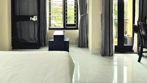 A hotel room with a large bed, a small table, and a window with curtains. - Flamingo Villa Hoi An (Da Nang)