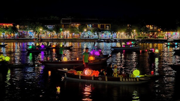 A nighttime river scene with boats and illuminated buildings along the shore. - Flamingo Villa Hoi An (Da Nang)