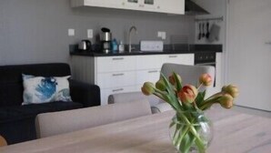 Una cocina moderna con armarios blancos, encimera negra y un comedor con un jarrón de tulipanes.