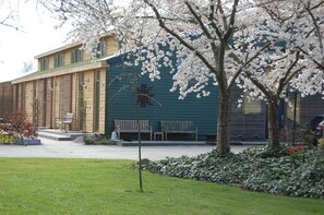 A building with a green exterior, wooden benches, and a tree with white blossoms. - Lelymare Logies (Lelystad)