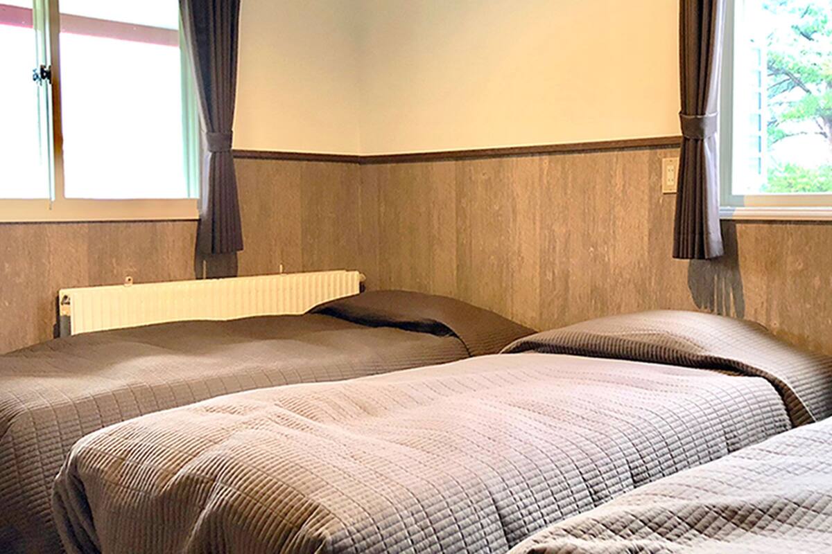 A room with two beds, a radiator, and a window with curtains.