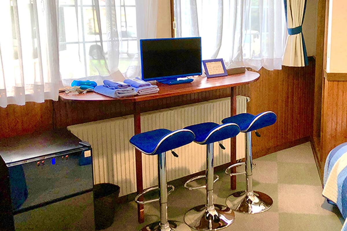 A hotel room with a bed, a desk with a computer, a chair, and a window with curtains.
