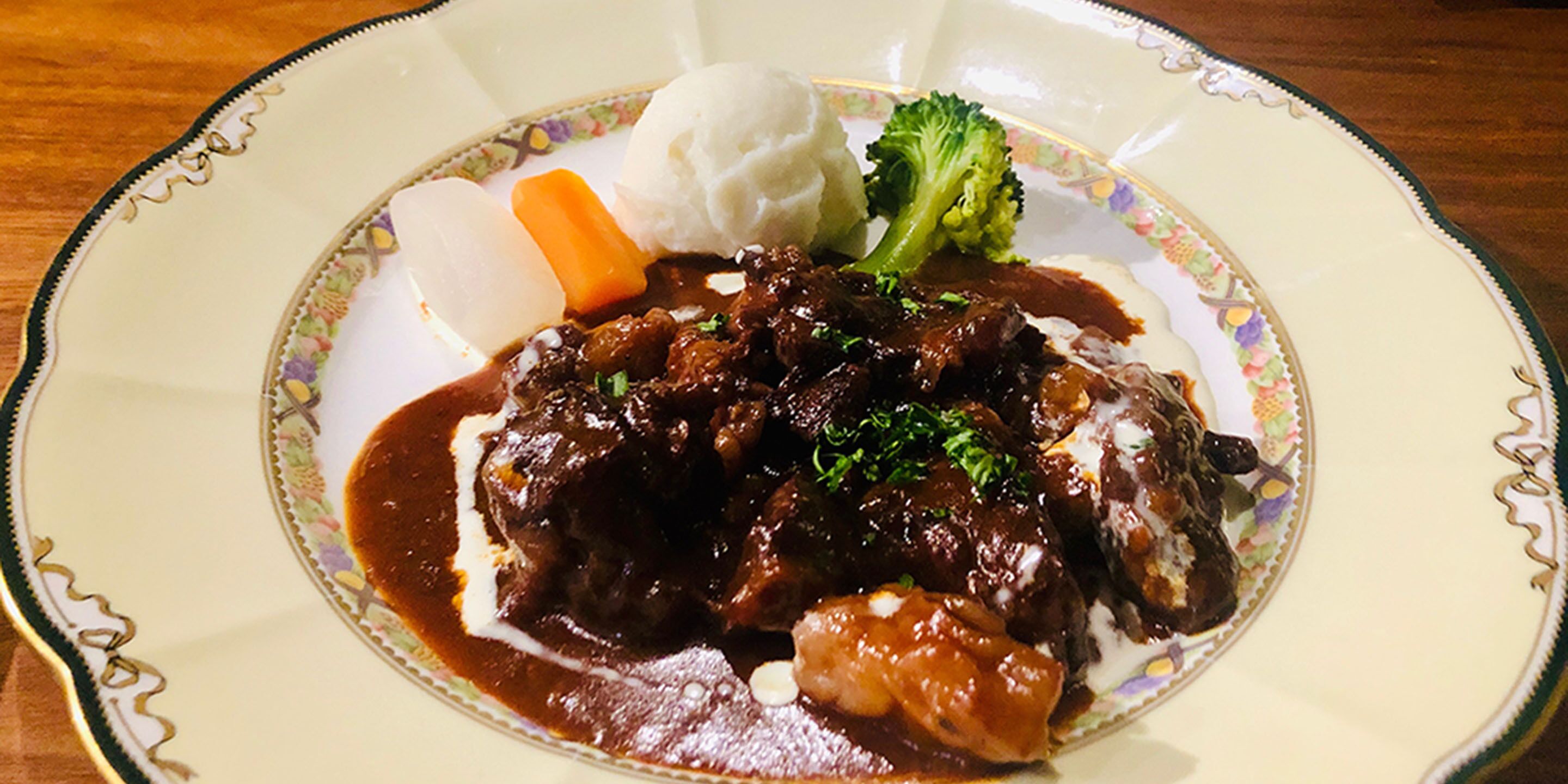 Een bord eten met een rundvleesgerecht, aardappelpuree, wortels en broccoli.