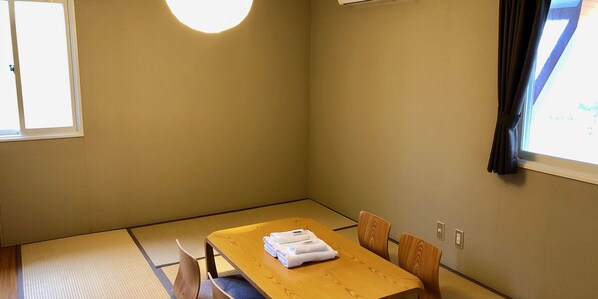 A room with tatami mat flooring, a wooden table with towels, and a window with curtains. - Arts Color (Hachimantai)
