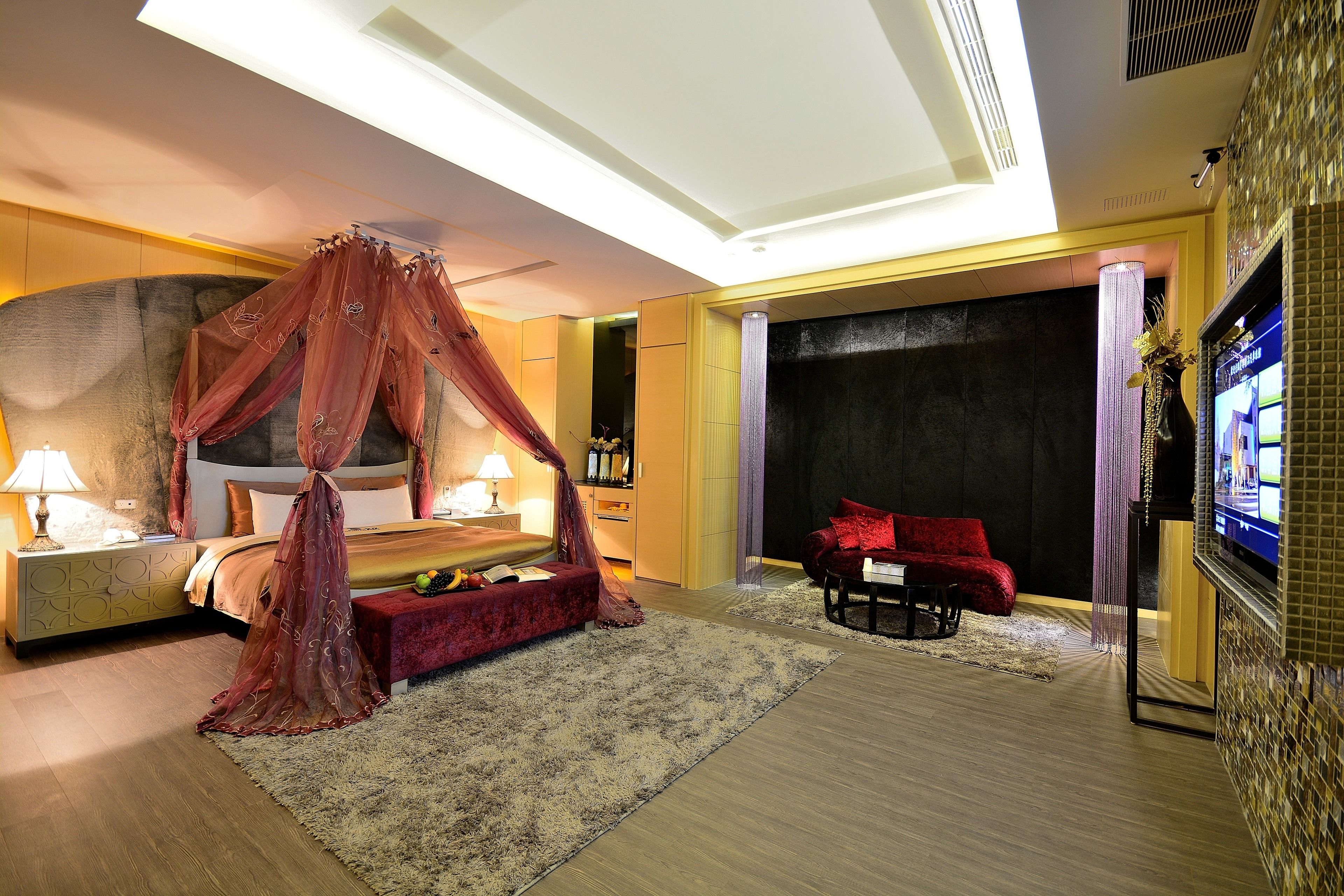 A bedroom with a four-poster bed, a red sofa, a TV, and a large window.