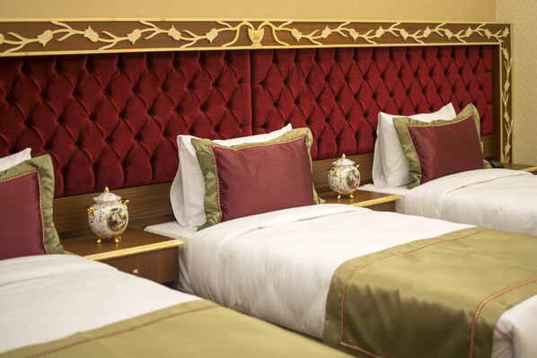 A hotel room with three beds, each with white bedding and green accents. The headboard is red with a decorative pattern.