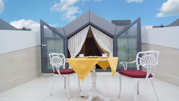 A modern outdoor dining area with a table and two chairs, a glass partition, and a clear sky. - MB Deluxe Hotel (Istanbul)