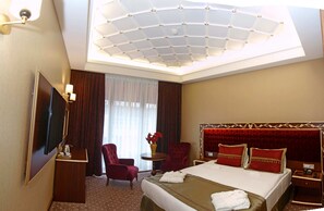 Habitación de hotel con una cama grande, un escritorio, un televisor de pantalla plana, una silla, una mesita con un florero y una lámpara del techo.