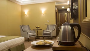 A hotel room with a bed, two armchairs, a small table with a bowl, and a plate of cookies. There is a kettle on the table. - MB Deluxe Hotel (Istanbul)