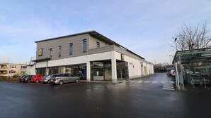 En moderne bygning med butiksvinduer og en parkeringsplads med flere biler.