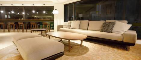 A modern living room with a sofa, ottoman, and coffee table, a patterned floor, and a large window with a view.