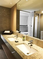 Un baño moderno con un espejo grande, dos lavamanos y una zona de ducha.