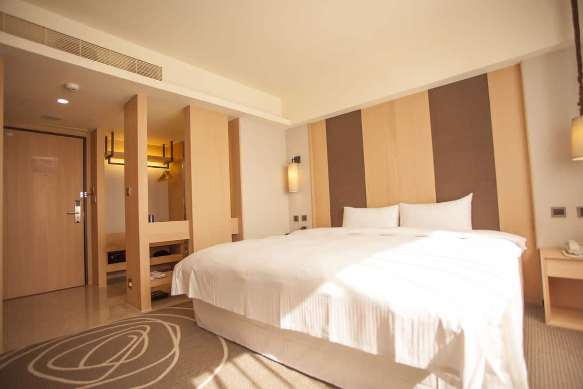 A hotel room with a large bed, a wardrobe, a desk, and a bathroom visible through an open door.