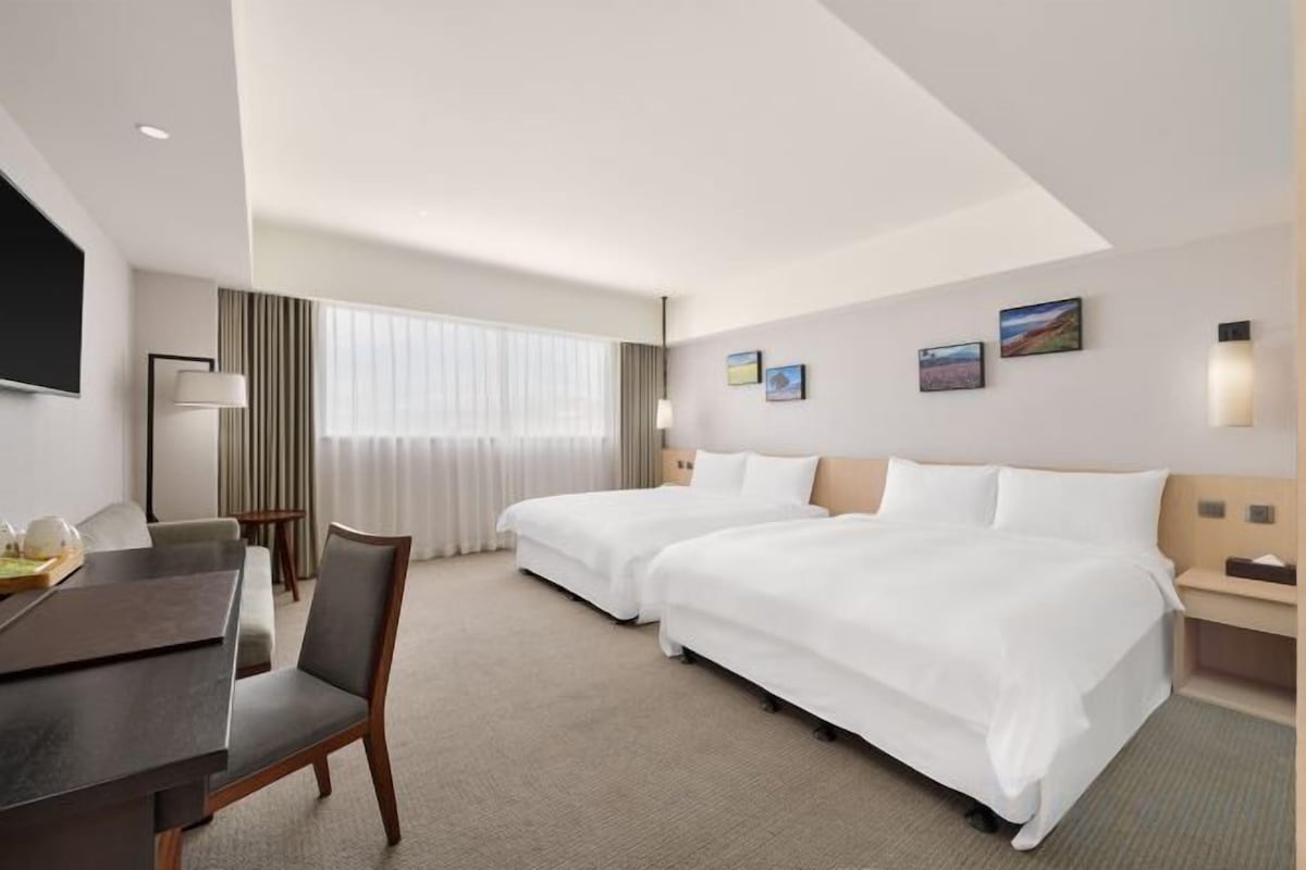 Une chambre d’hôtel avec deux lits, un bureau, une chaise, une télévision et une fenêtre avec des rideaux.
