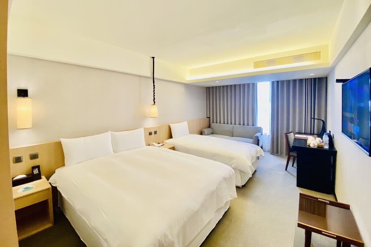 A hotel room with two beds, a desk, a chair, a television, and a window with curtains.