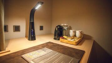 A hotel room with a bedside table, a lamp, a coffee maker, and a tray with tea and snacks.