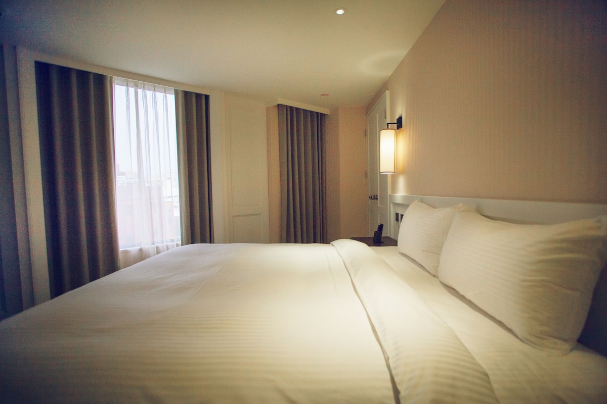 A hotel room with a large bed, a nightstand, a lamp, and a window with curtains.
