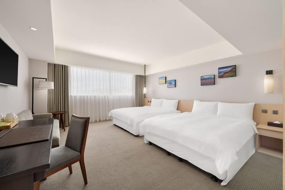 A hotel room with two beds, a desk, a chair, a TV, and a window with curtains.