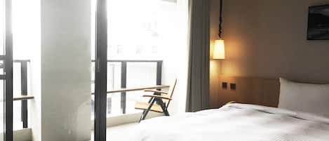 A hotel room with a bed, a chair, a balcony, and a wall-mounted lamp.
