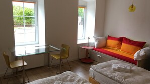 A modern bedroom with a glass desk, yellow chair, two beds, a red and orange sofa, and large windows. - Alte Post Greifenstein (Sankt Andrae-Woerdern)