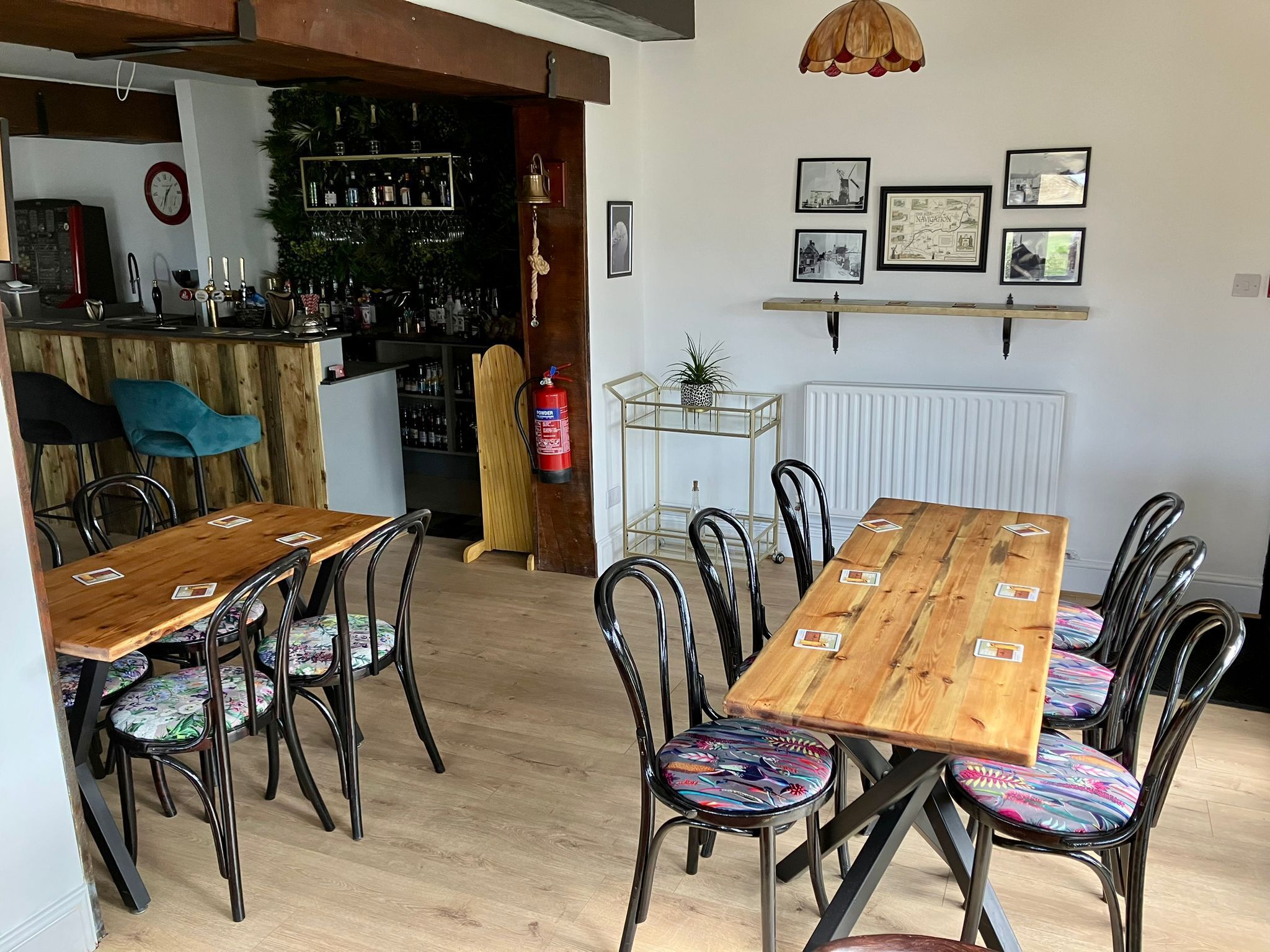 A dining area with a wooden table and chairs, a bar in the background, and wall-mounted pictures.