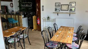 A dining area with a wooden table and chairs, a bar in the background, and wall-mounted pictures.