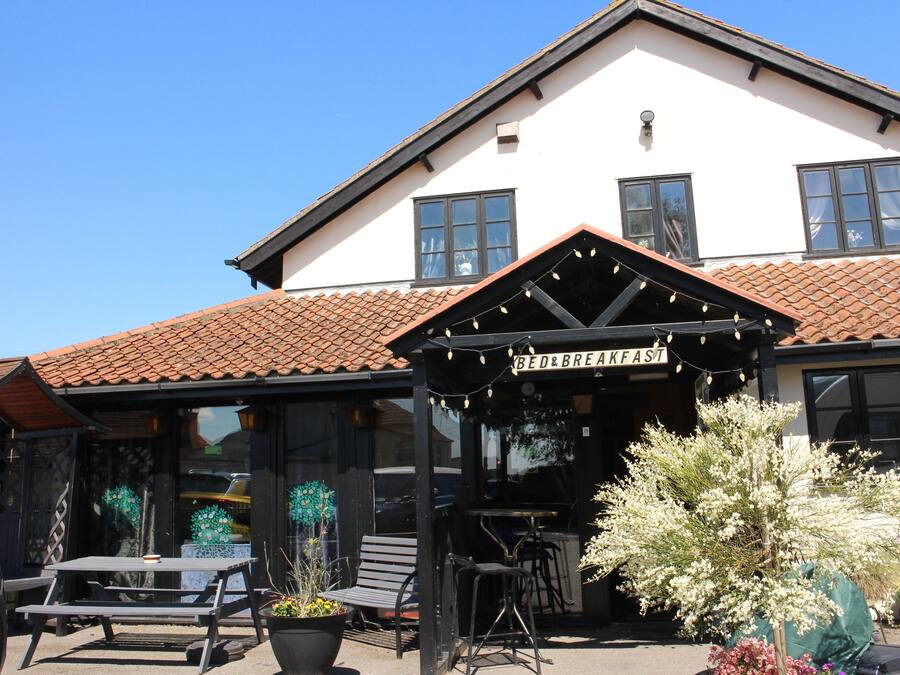 En bygning med skilt, der siger "BED & BREAKFAST", og en patio med borde og stole.