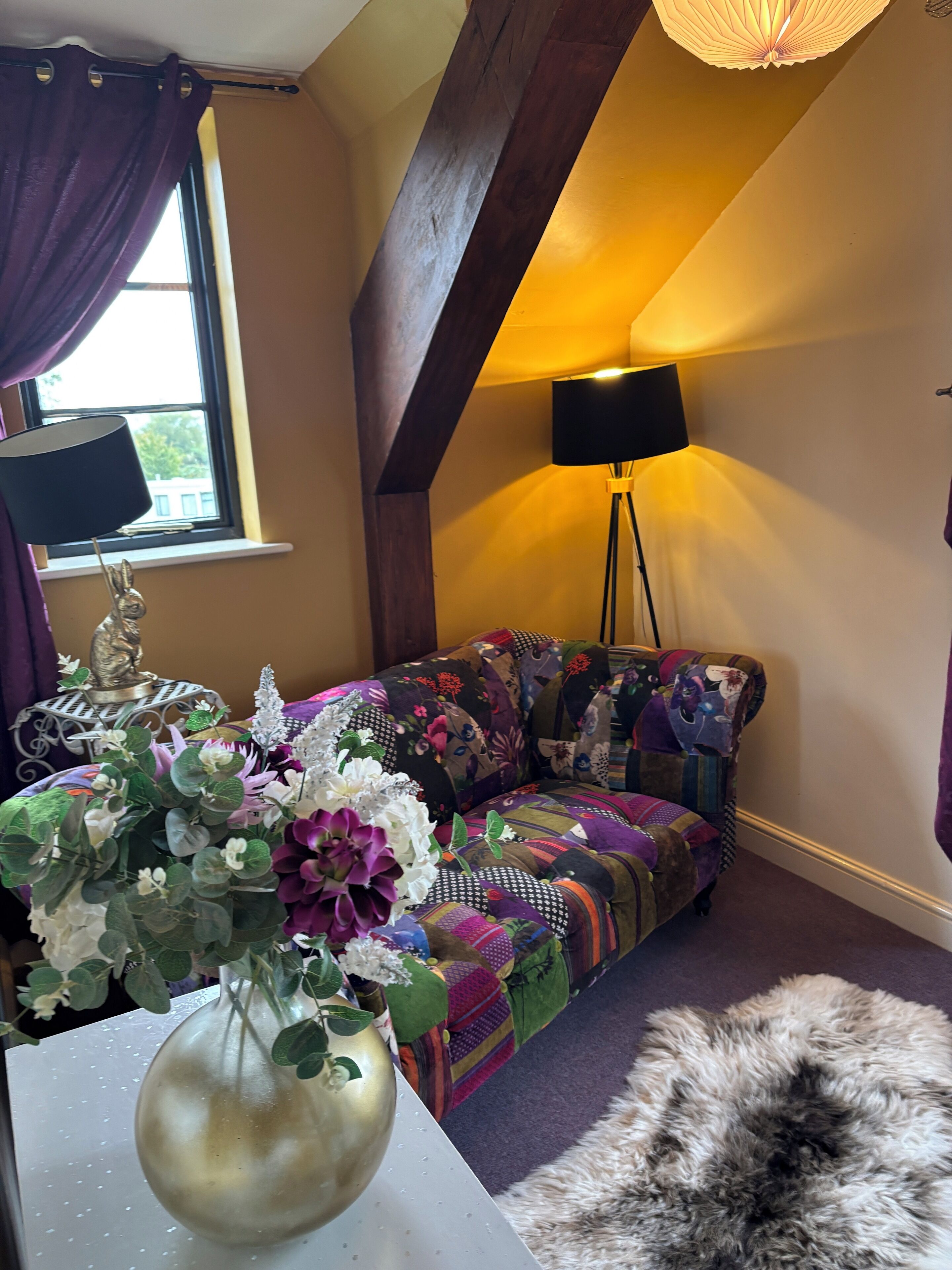 A cozy room with a colorful sofa, a decorative vase with flowers, and a lamp.