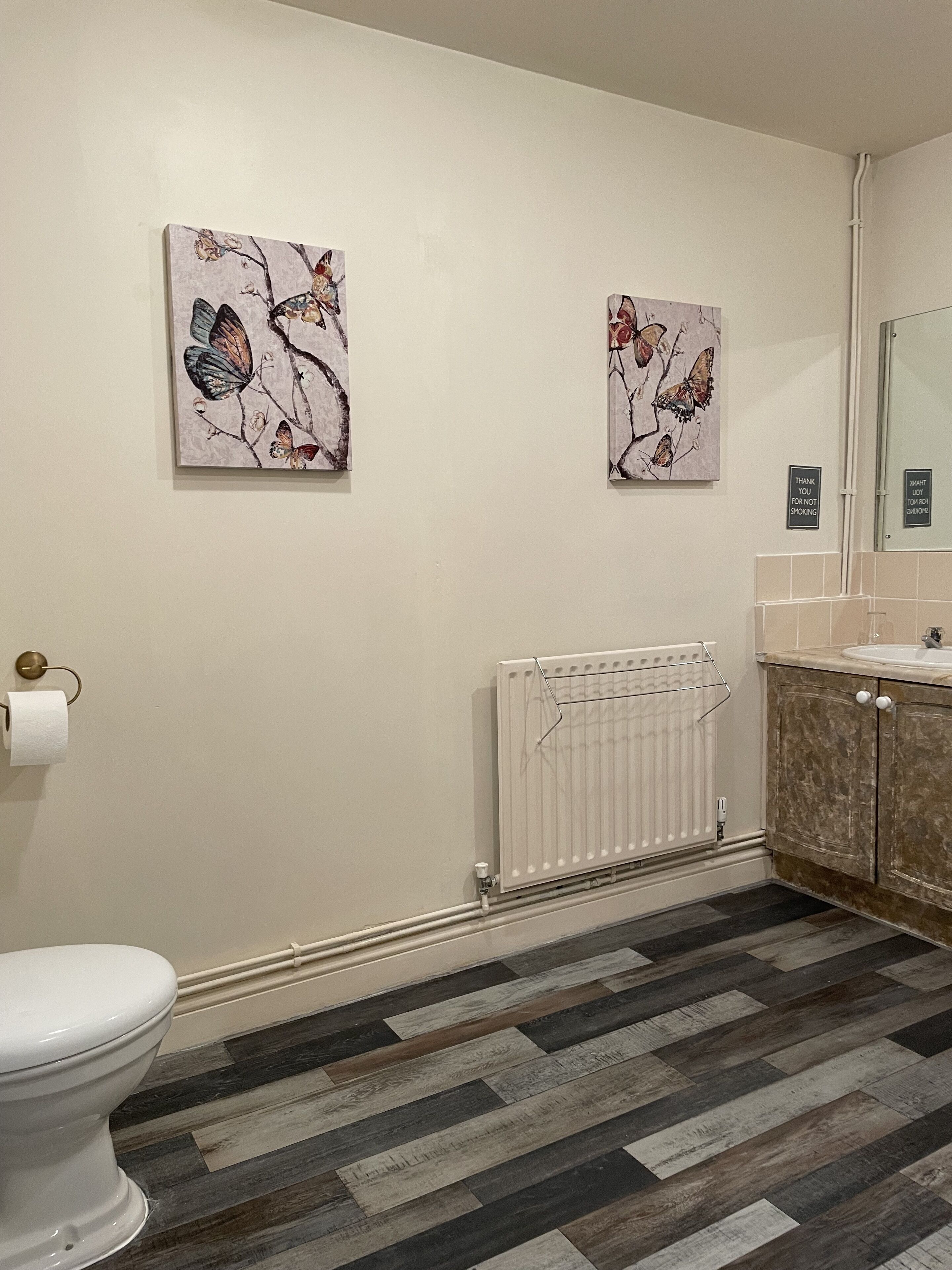 Un baño con inodoro, un radiador y dos obras de arte con motivo de mariposas en la pared.