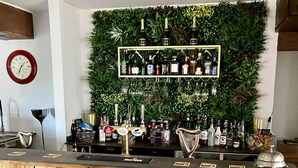 A bar area with wooden bar counter, two chairs, a clock, and a wall decorated with plants and bottles. - The Crown Lodge Bar Bed & Breakfast  (Lincoln)
