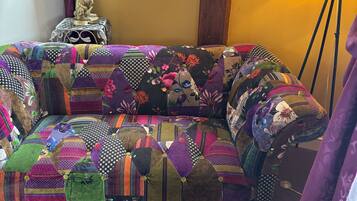 A cozy room with a colorful, patchwork sofa, a small table with a rabbit statue, and a window with curtains.