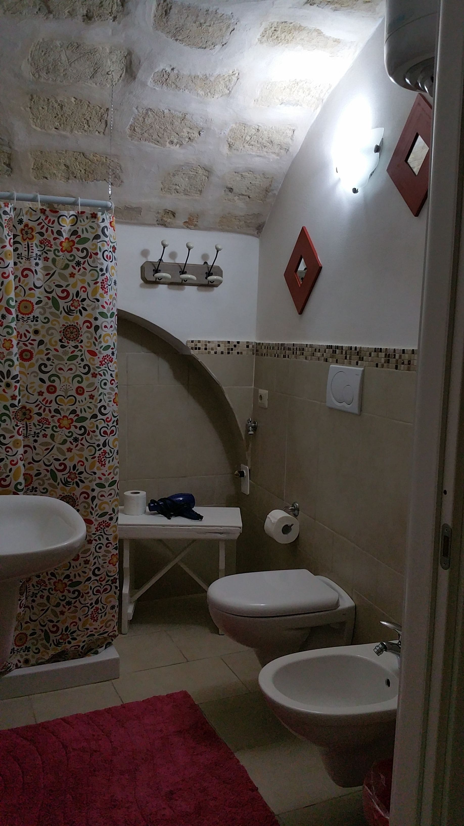 A bathroom with a shower curtain, a toilet, a bidet, and a sink.