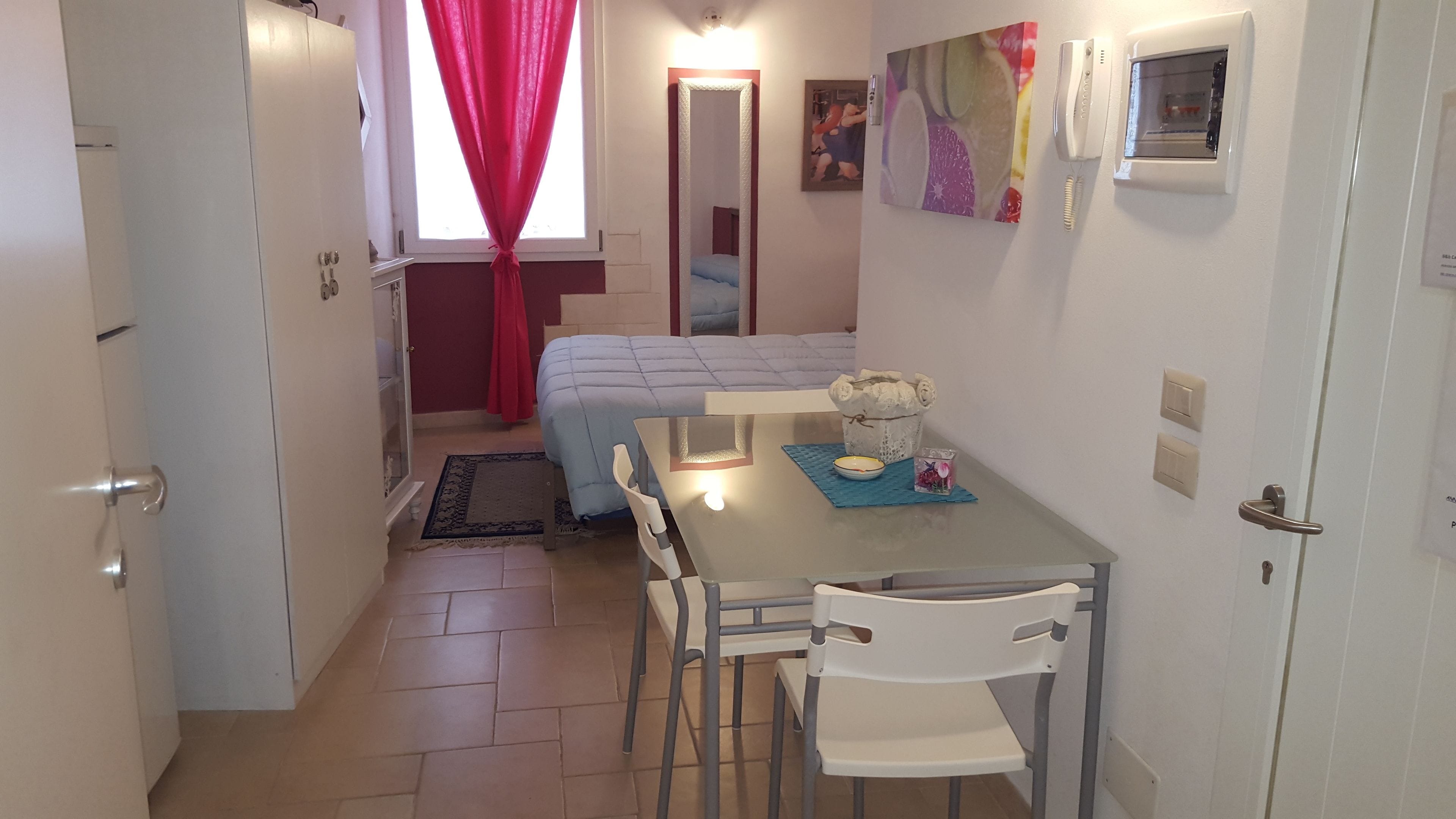 A compact room with a bed, a small table with chairs, a telephone, and a painting on the wall.