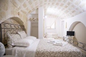 Una camera da letto con un arco in pietra, un letto con testiera in metallo, una televisione su un tavolino e una finestra con tende.