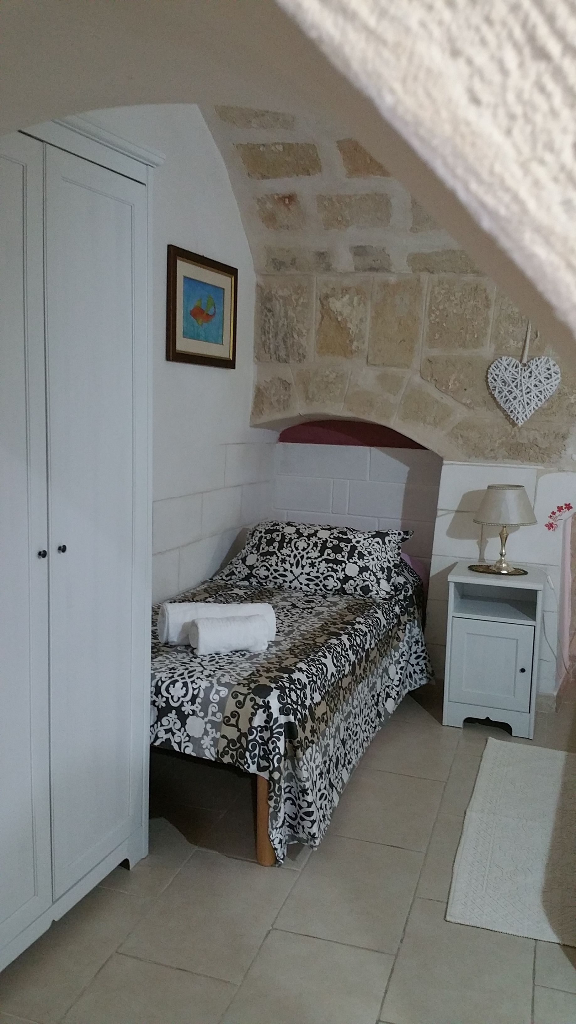 Una camera da letto con un letto, un armadio, un comodino, una lampada, un portafoto e una decorazione a forma di cuore sulla parete.