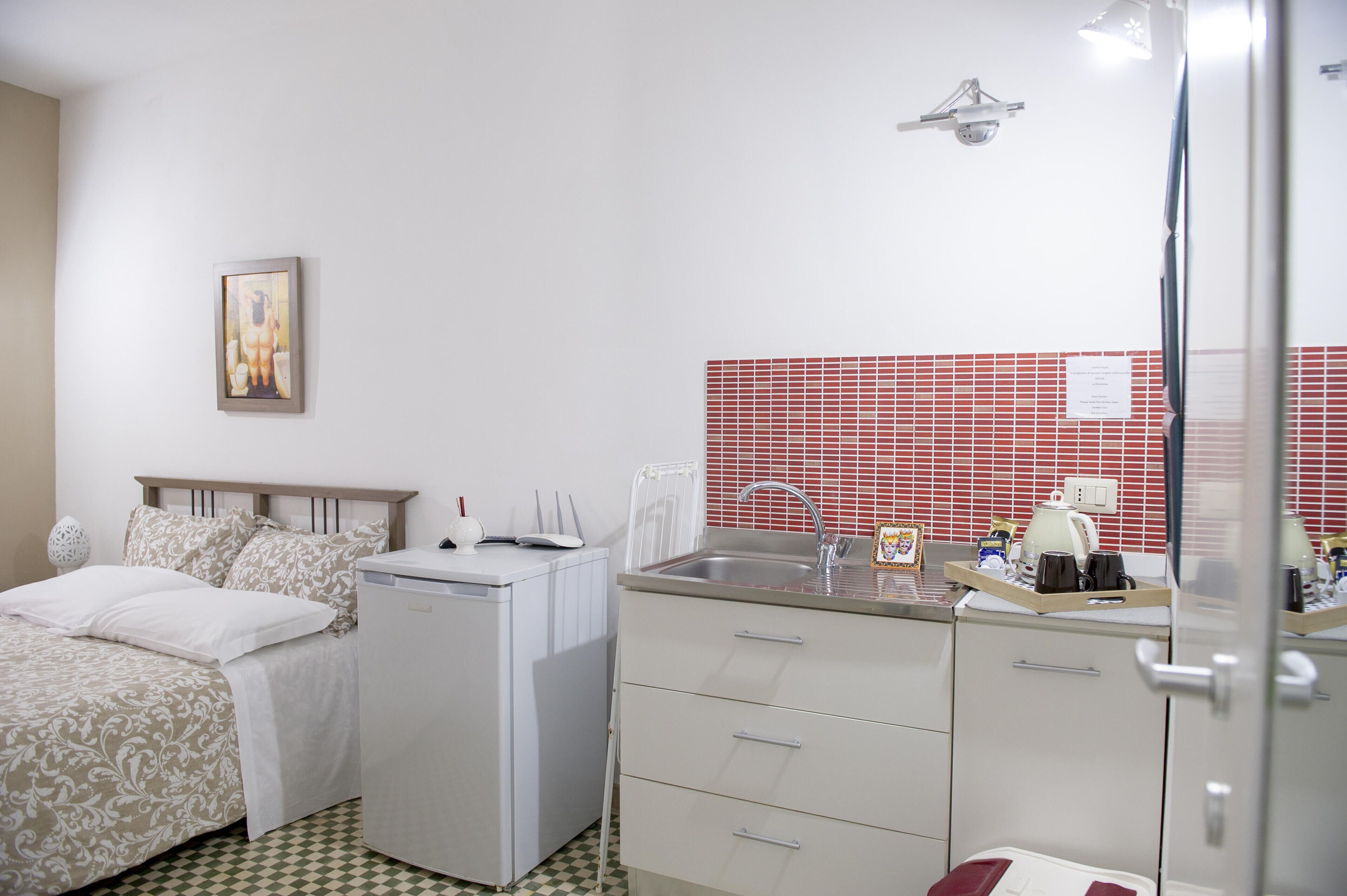 A compact hotel room with a bed, a small kitchenette, a sink, and a mirror.