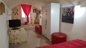 A room with a television on a white table, a red sofa, a red curtain, a white wardrobe, and a painting on the wall. - Casa Nave (Monopoli)