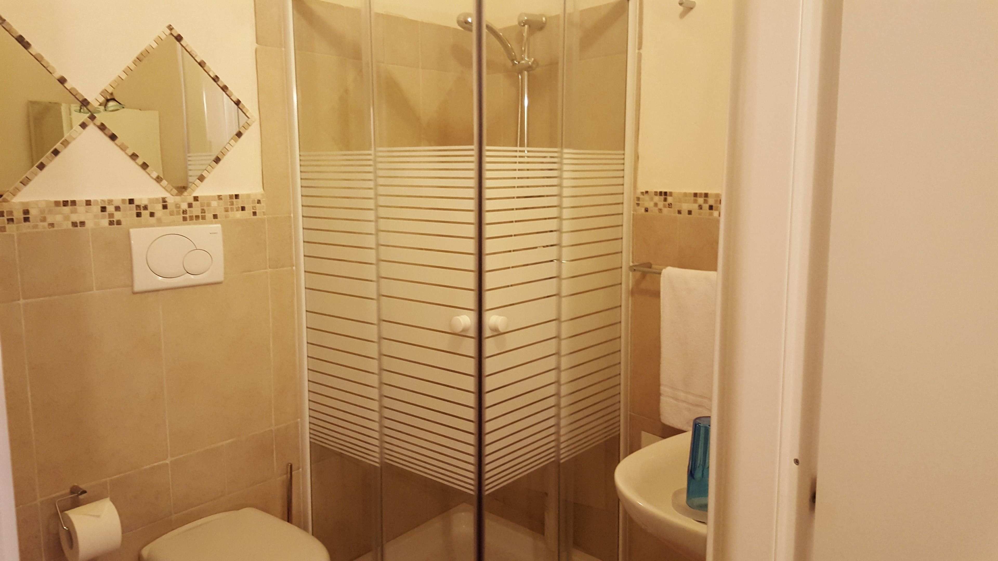 Un bagno con cabina doccia in vetro, un water e un lavandino con dispenser di sapone blu.