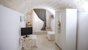 A room with a stone ceiling, a white wardrobe, a small table with a TV, and a window with a curtain. - Casa Nave (Monopoli)