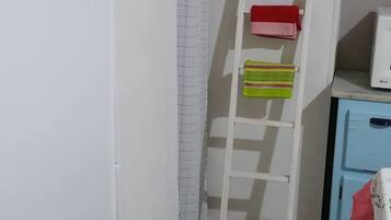 Ein schmales Badezimmer mit einem weißen Waschbecken, einer weißen Toilette, einem weißen Regal mit einem roten Handtuch, einer weißen Hockerleiter und einem weißen Vorhang.