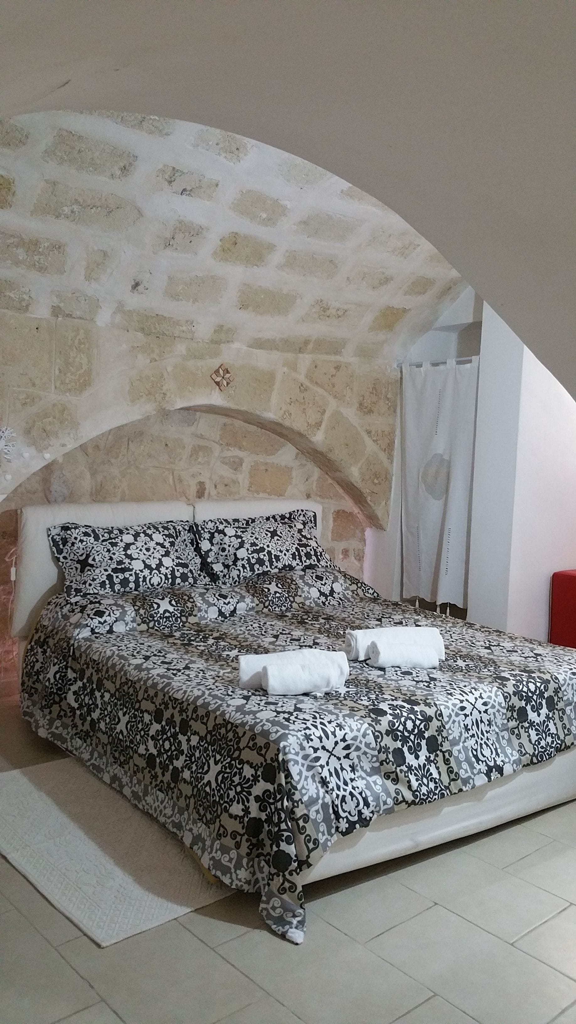 Una cama con una colcha estampada, un almohadón y dos toallas enrolladas.