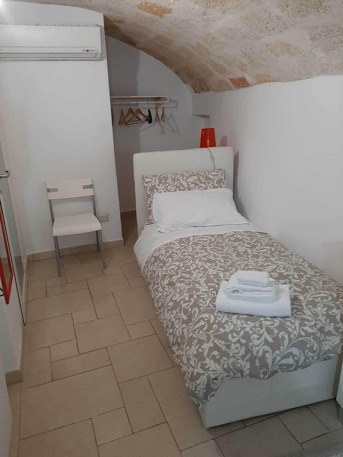 A small, clean room with a bed, a chair, and a wardrobe.