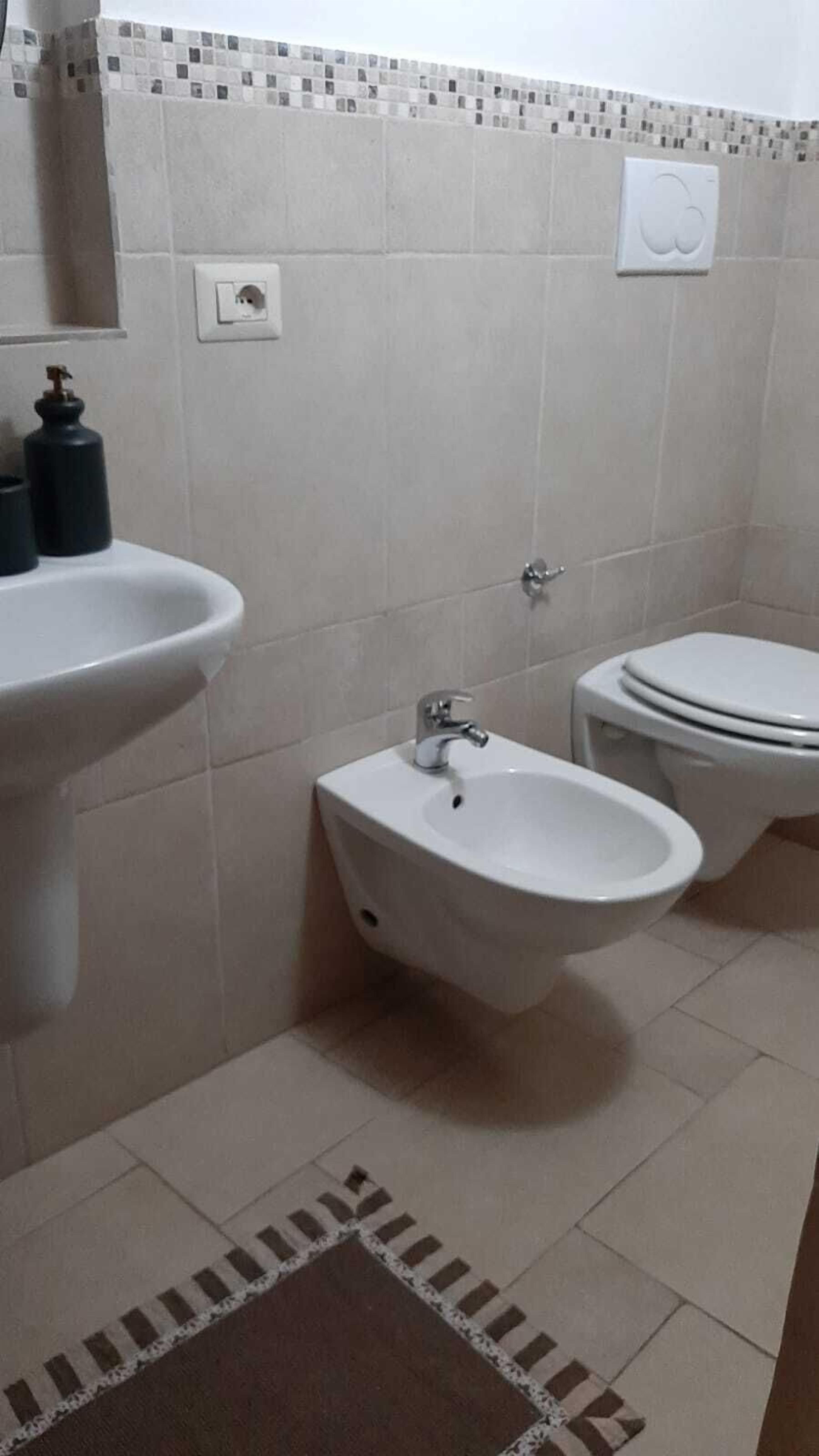 Ein Badezimmer mit Waschbecken, Bidet, Toilette und einer gefliesten Rückwand.